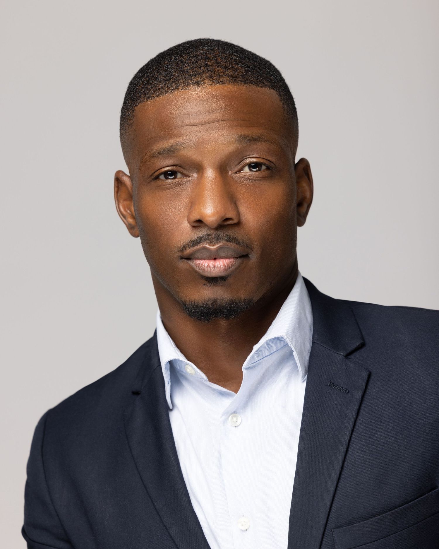 Professional headshots of a man in a navy suit and white shirt against a gray background.