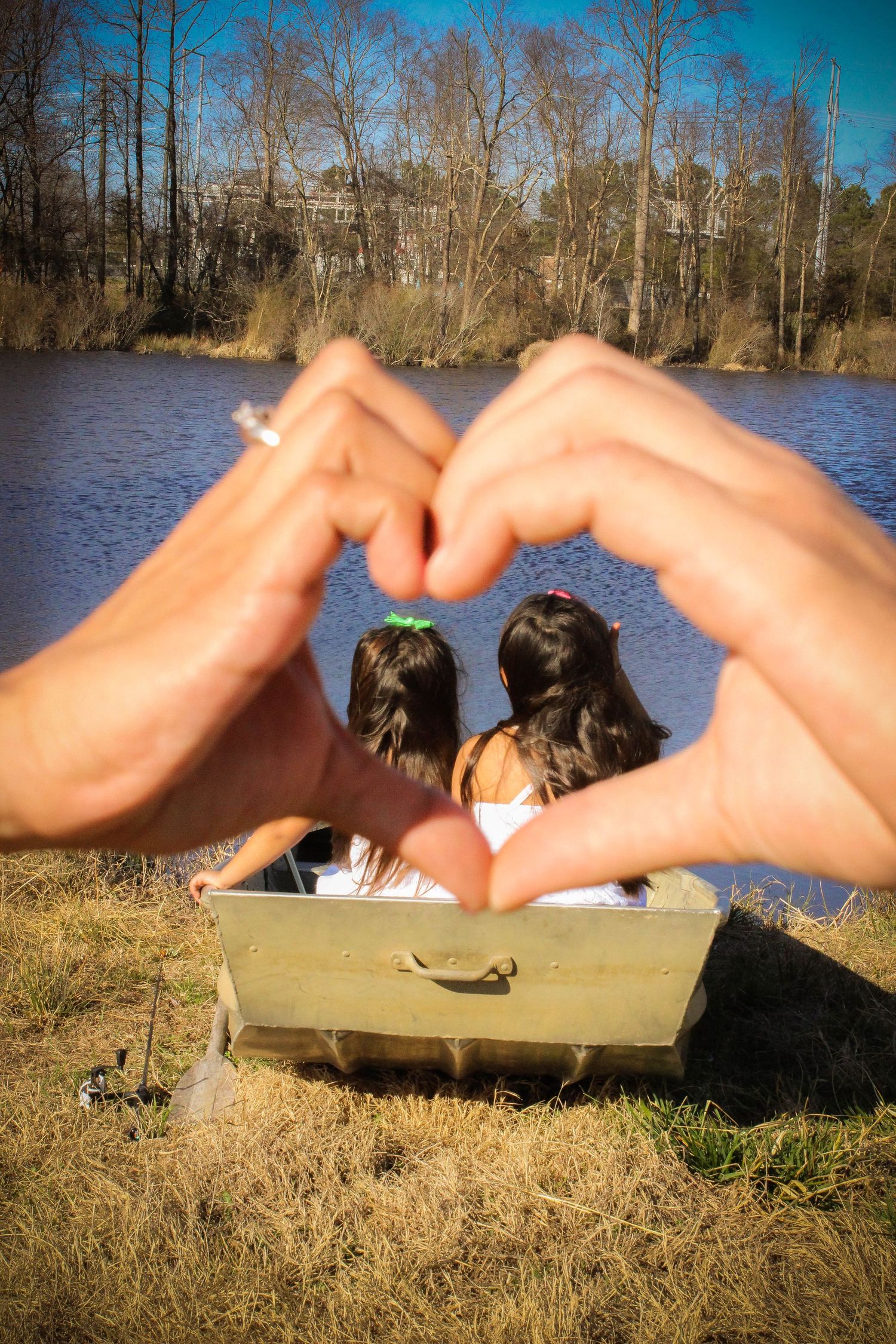 Hands forming heart shape frame against lake and trees in romantic outdoor scene.