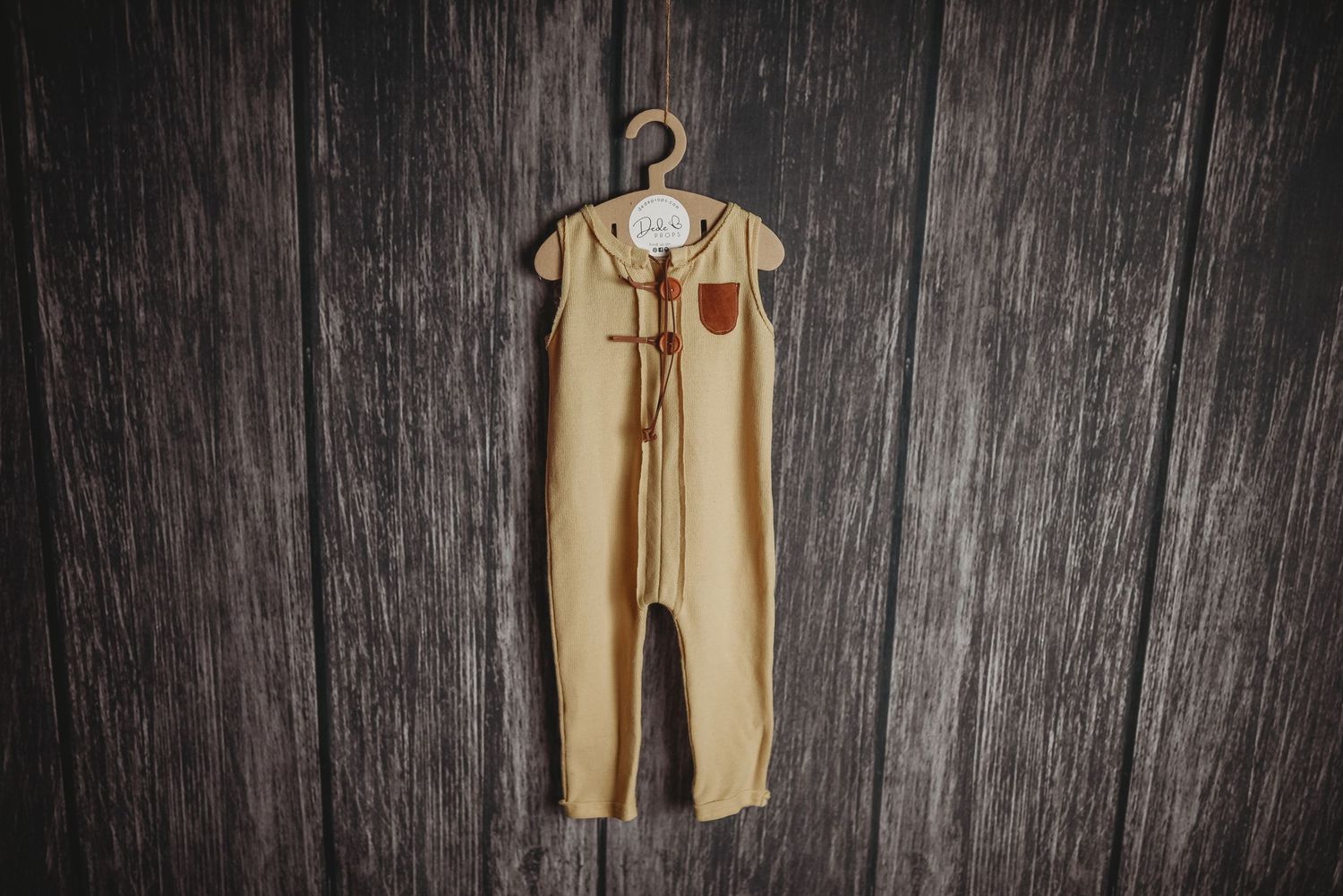 Beige baby romper with ruffled details hanging against dark wooden background.