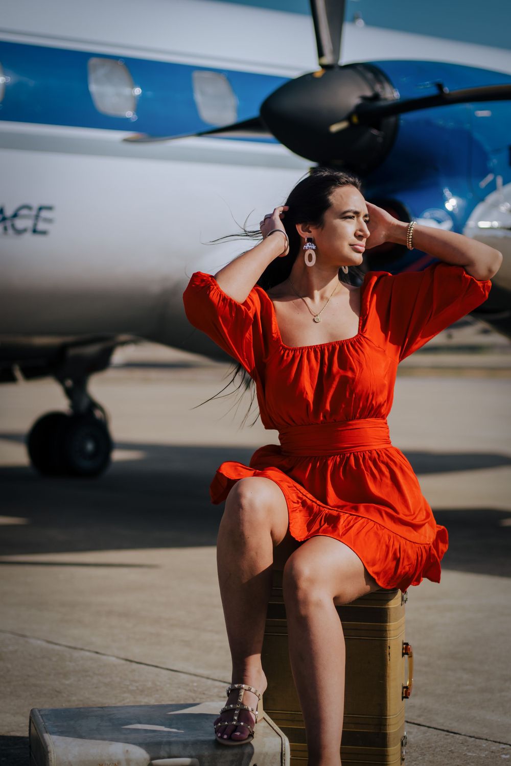 Woman in vibrant red dress poses outdoors near parked aircraft on tarmac.