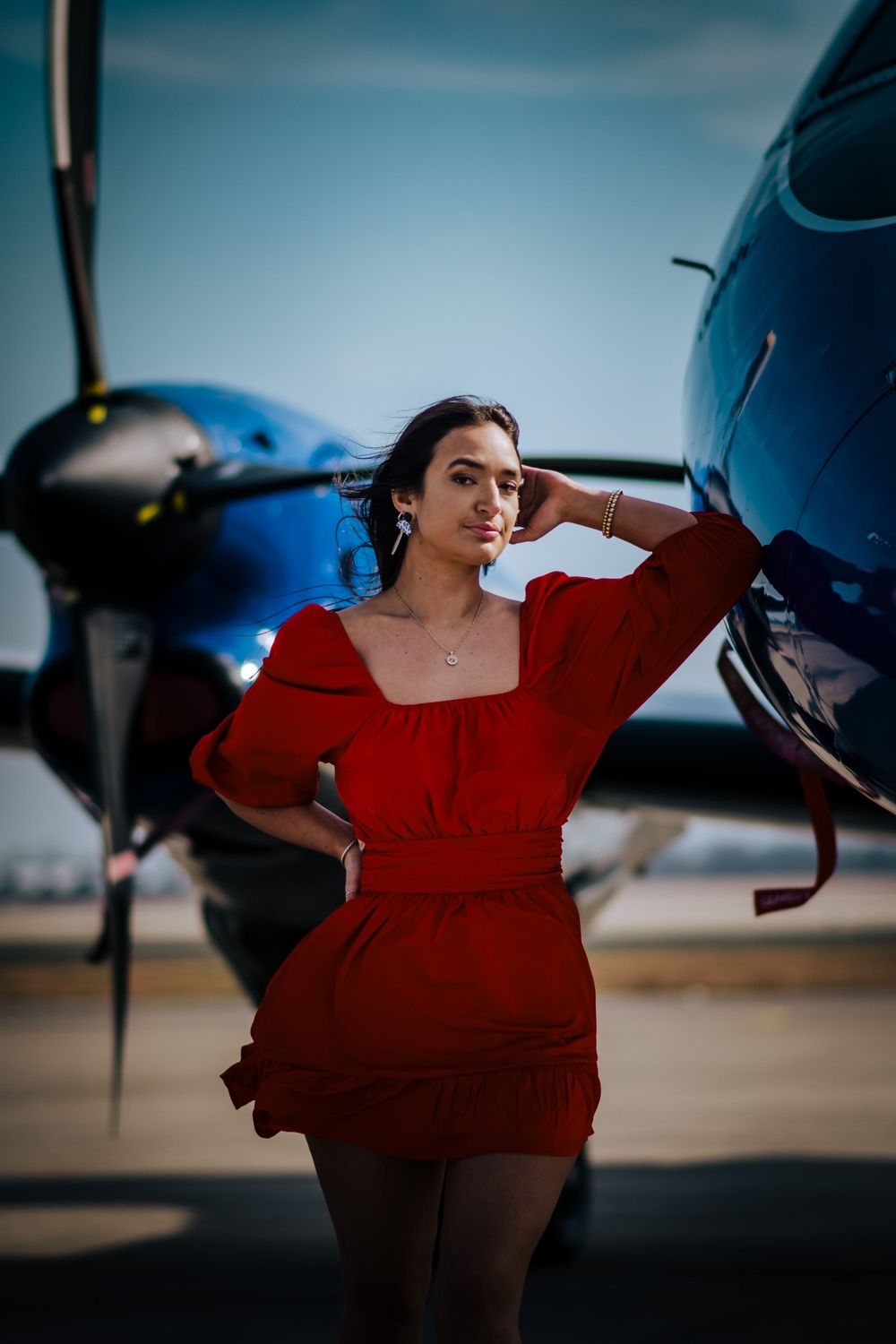 Fashion shoot featuring red dress against blue and white aircraft backdrop.