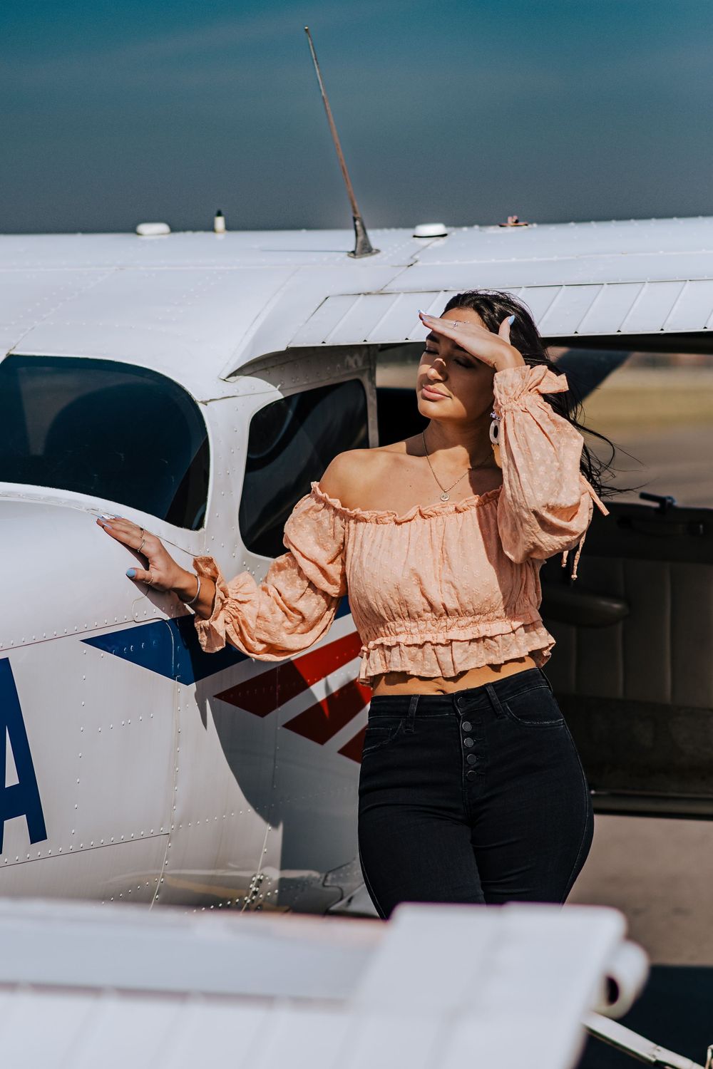 Person in peach blouse inspecting wing of small white aircraft on airfield.