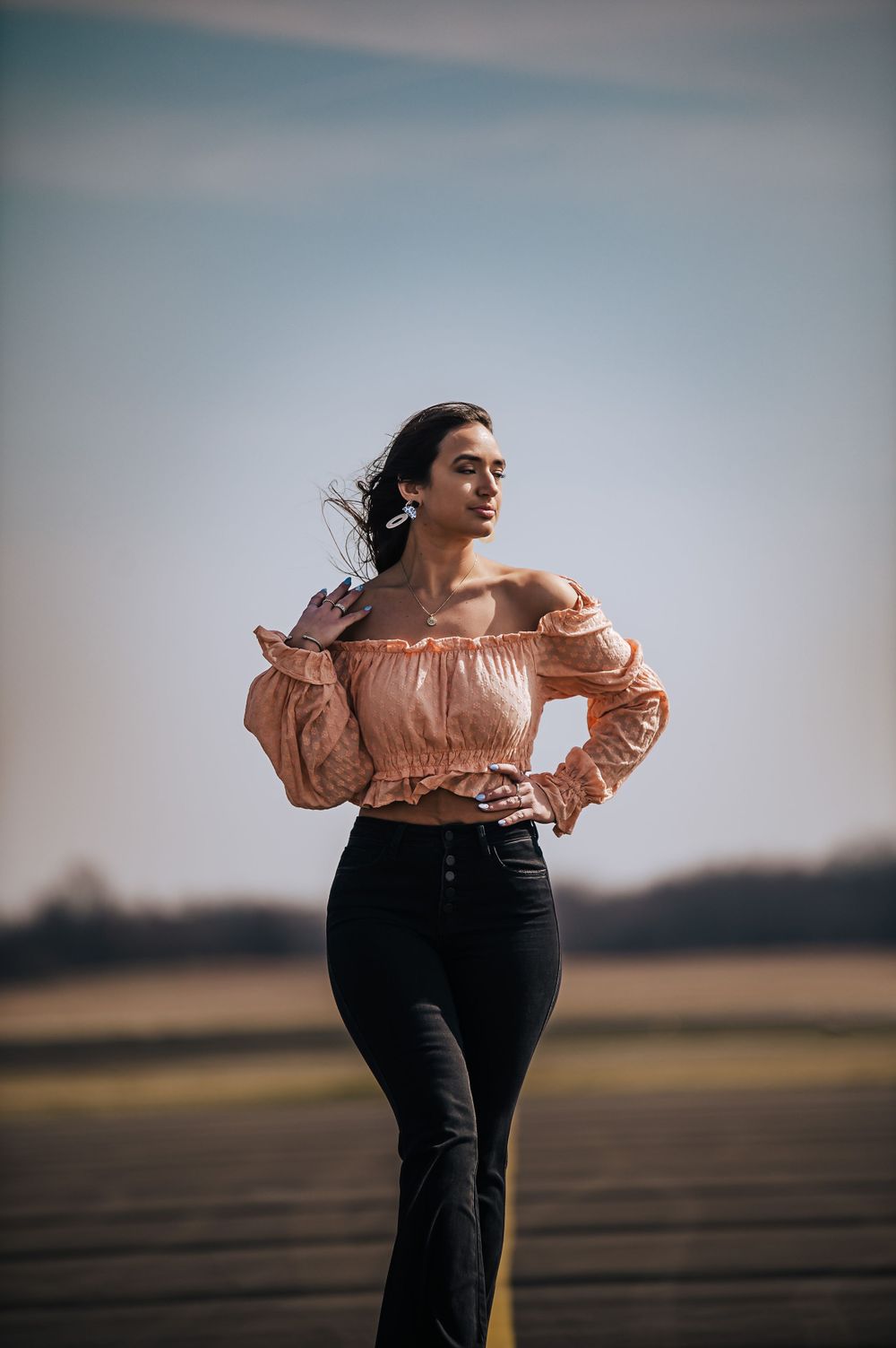 Stylish outfit captured in motion against blurred rural landscape at sunset.