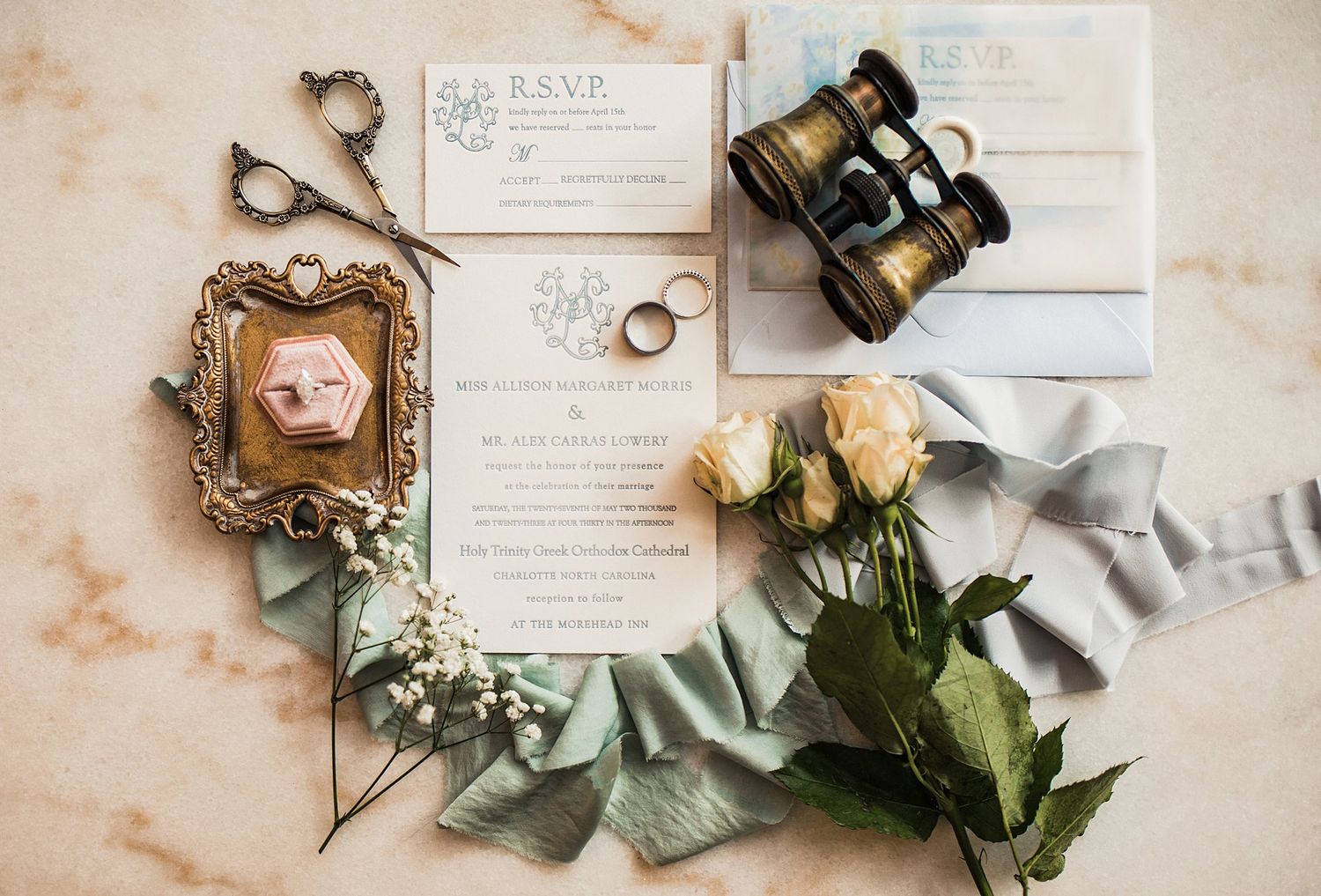 Wedding details arranged with RSVP card, vintage frame, binoculars and roses on marble background.