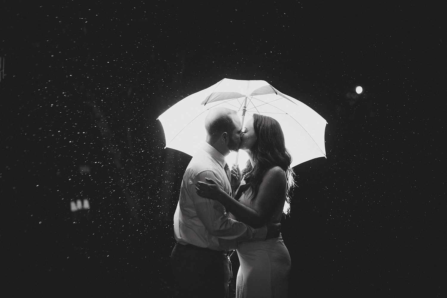 Romantic nighttime portrait under white umbrella with rain and moonlight creating dreamy atmosphere.