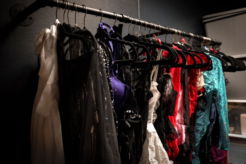 Rack of elegant formal dresses in various colors hanging in a dark room.