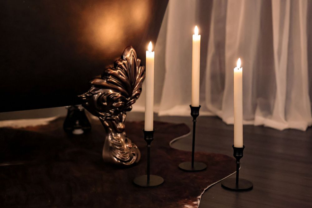 Three black candlesticks with white candles beside decorative crystal ornament.