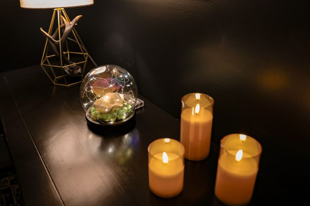 Modern geometric lamp with glass terrarium and lit candles on dark surface.
