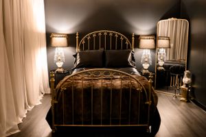 Elegant bedroom with brass bed frame, matching table lamps, and flowing curtains in moody lighting.