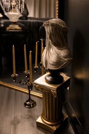 Classical marble bust statue on ornate pedestal with golden candles creating dramatic ambiance.