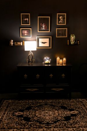 Dark room with gallery wall, vintage dresser, and decorative candles creating moody atmosphere.