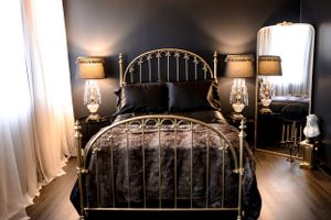 Modern bedroom featuring metallic bed frame, crystal lamps, and floor mirror in dark tones.