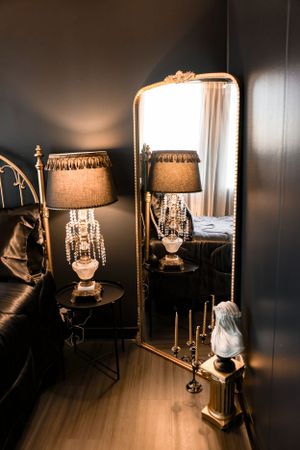 Elegant floor mirror reflecting crystal table lamp and decorative elements in warm lighting.