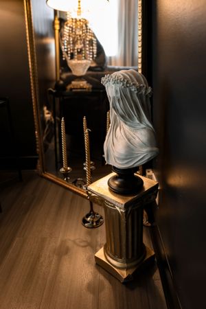 Decorative marble bust on classical column with mirror reflection and candlesticks in moody lighting.