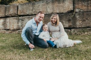 A family sits together on grass against a stone wall background during an outdoor photo session.