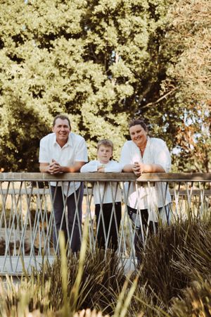 Three people lean against a wooden railing overlooking a scenic garden landscape.