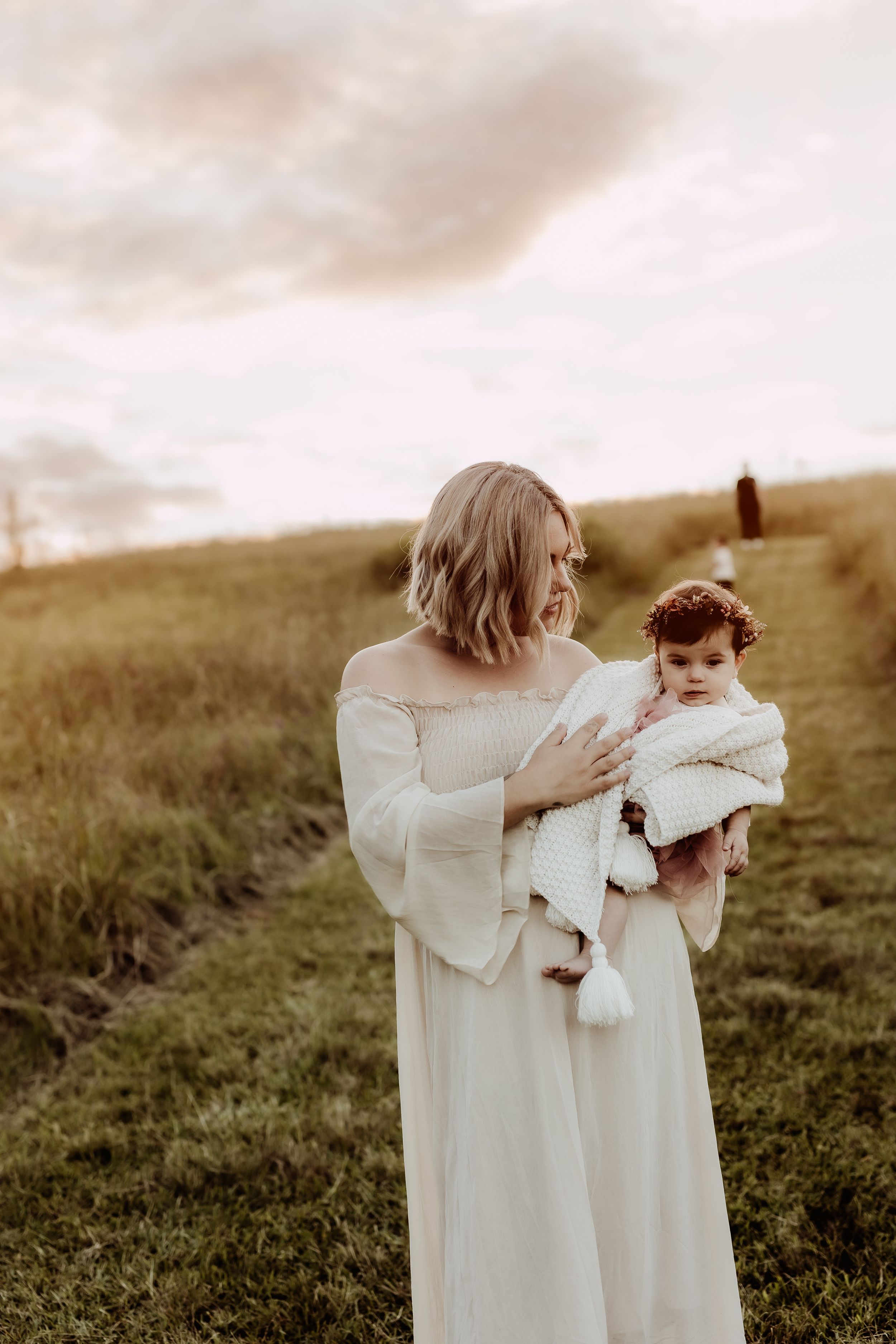 Two people in flowing white dresses embrace in a sunlit meadow.