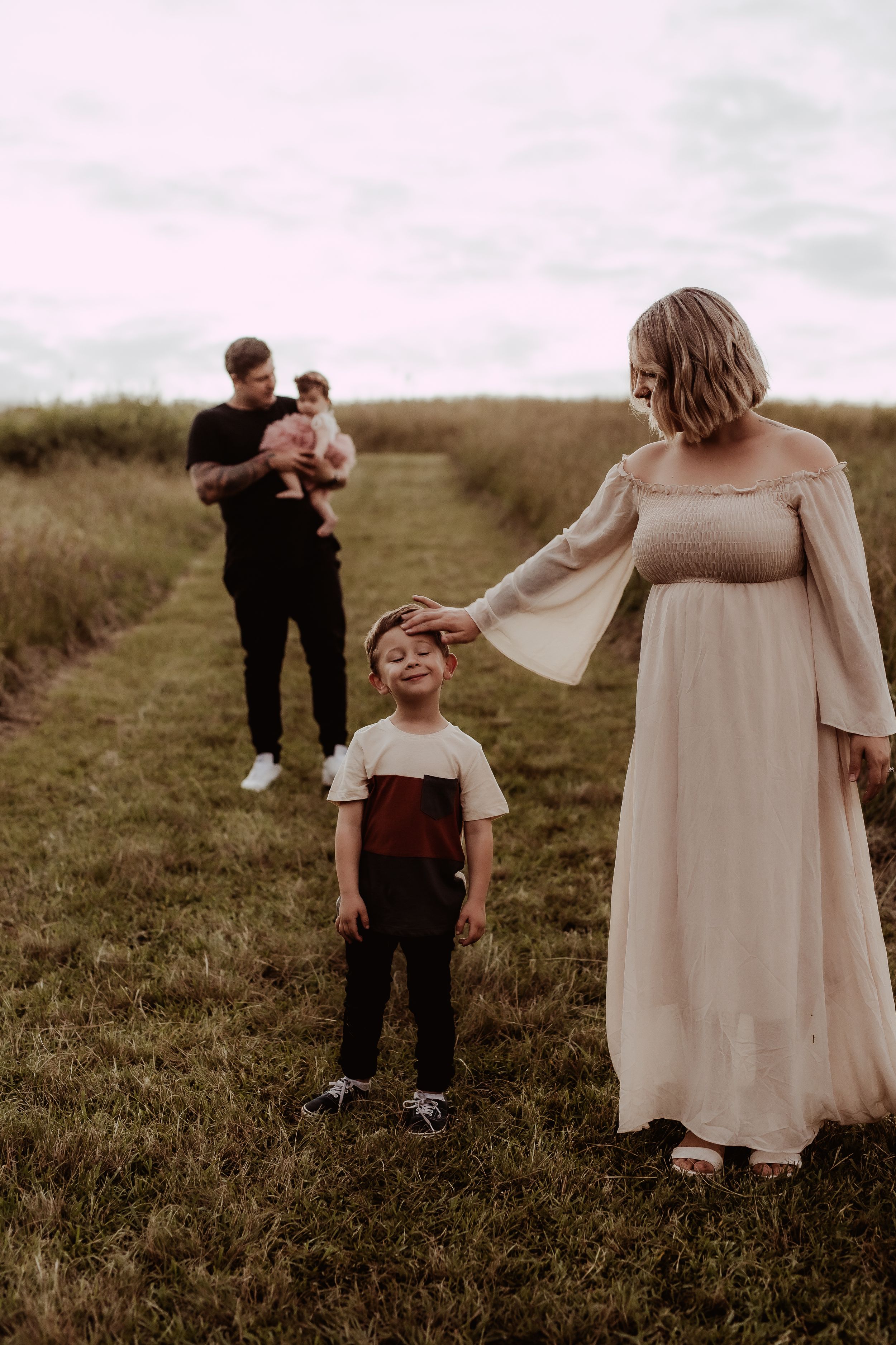 Family members share intimate moments together in a grassy field at dusk.