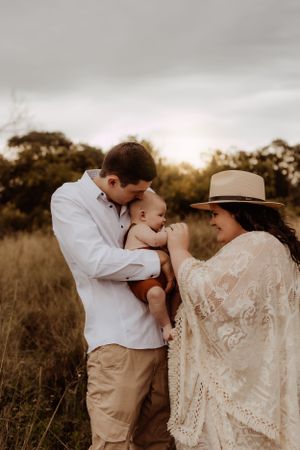 Family shares intimate kisses during sunset portrait session in natural field setting.