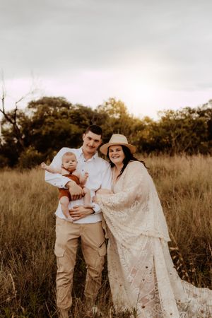 Family poses together in rustic field setting during golden hour photo session.