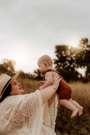 Family shares playful moment lifting baby during outdoor sunset photoshoot.