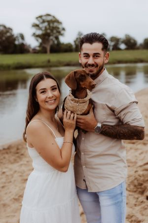 Couple shares playful moments on sandy beach near lake during golden hour photo session.