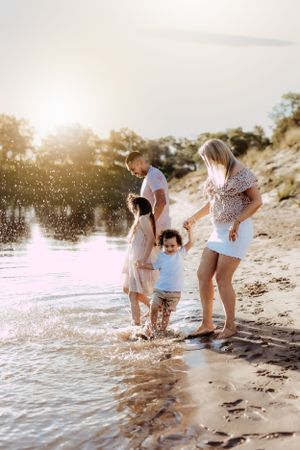 Family playing and splashing in shallow water during a beach photoshoot.