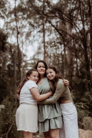 Three sisters embrace in heartfelt moment during outdoor photo session.