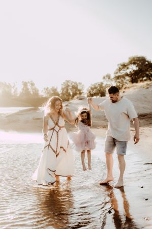Family plays together in shallow water at beach during sunset photo session.