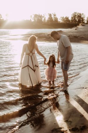 Family creates memories together while splashing in beach water at golden hour.