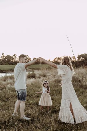People in white and casual clothing dance together in a meadow at golden hour.