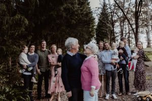 Extended family gathering poses together outdoors among trees.