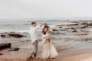 Couple embracing on a rocky beach shoreline with waves crashing behind them.