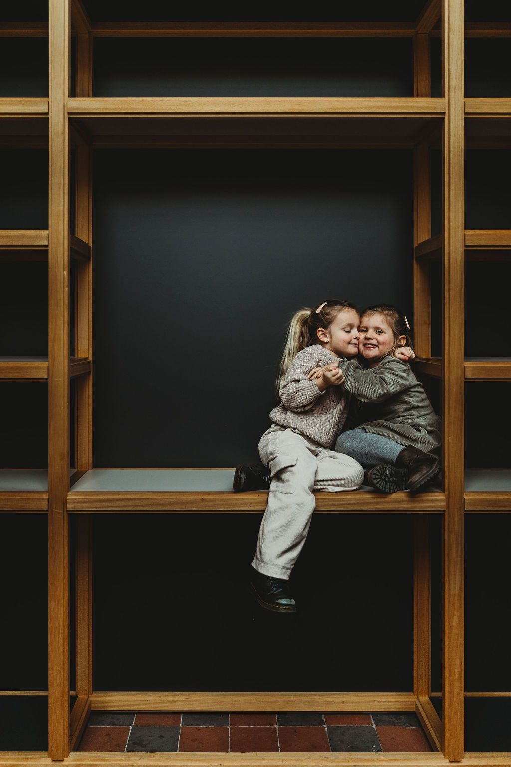 Two children sharing sweet moment sitting in wooden cubby shelf.