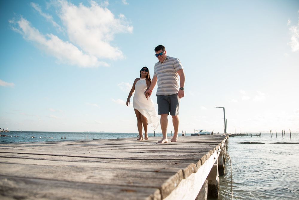 Maureen and John walking hand-in-hand on a wooden dock at a beach club in Isla Mujeres, Mexico