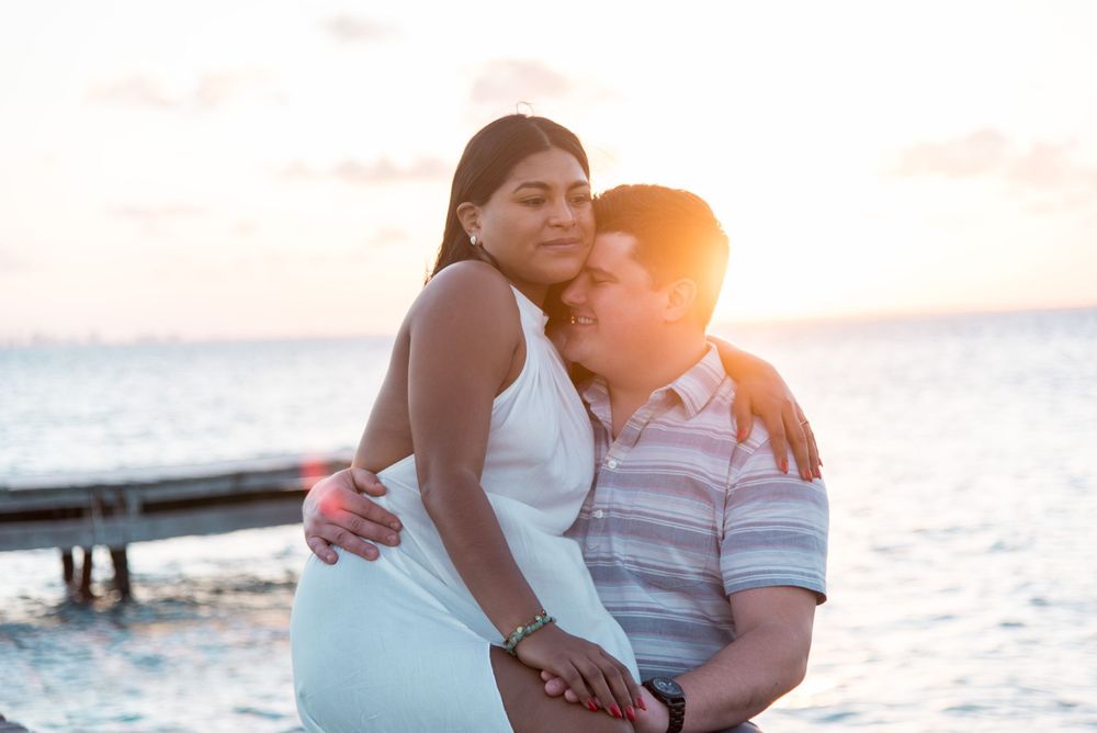 Maureen and John sitting by the dock with the sunset of Isla Mujeres behind them