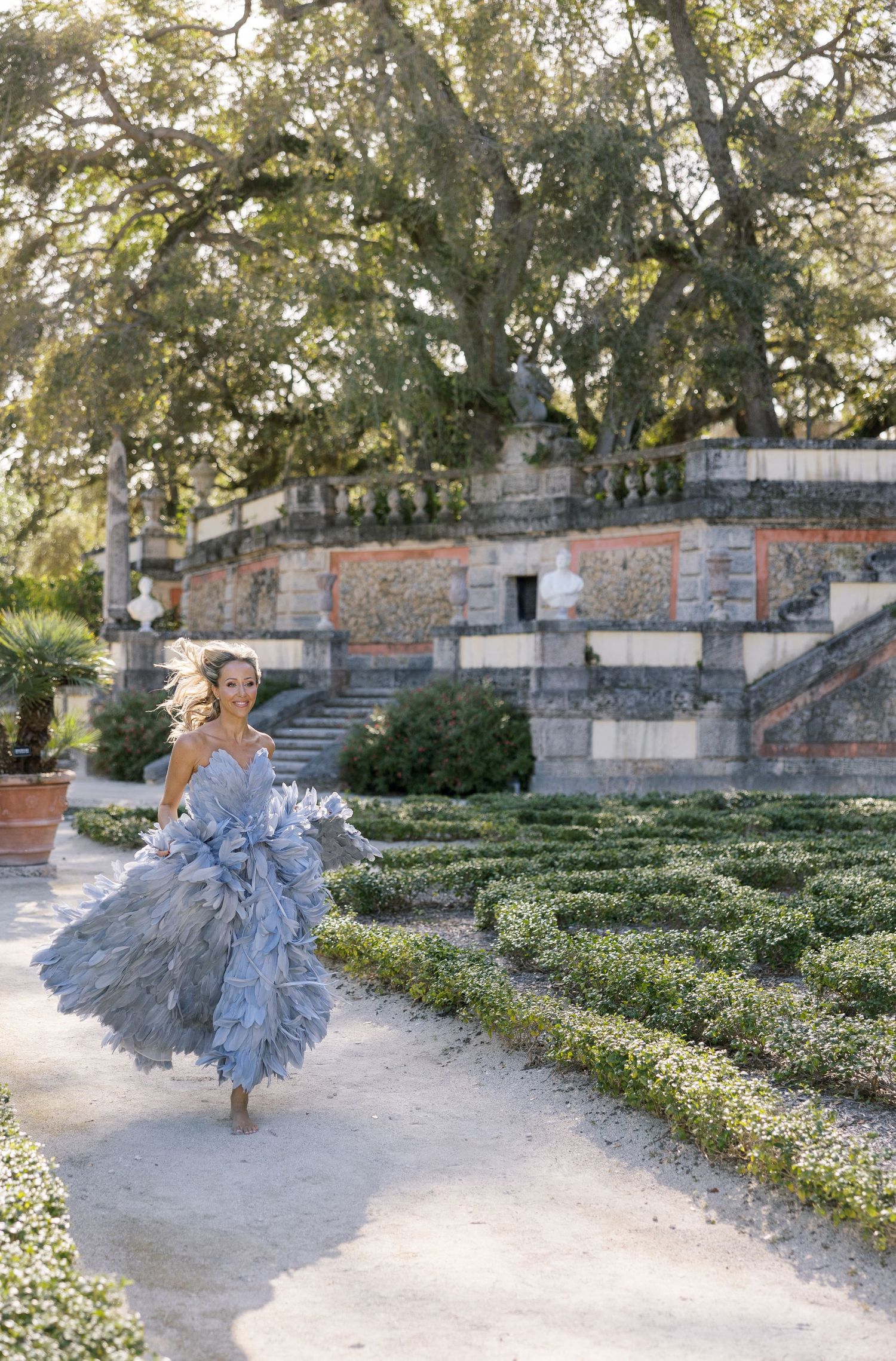 An ethereal fashion photo featuring a flowing gray dress in a formal garden setting.