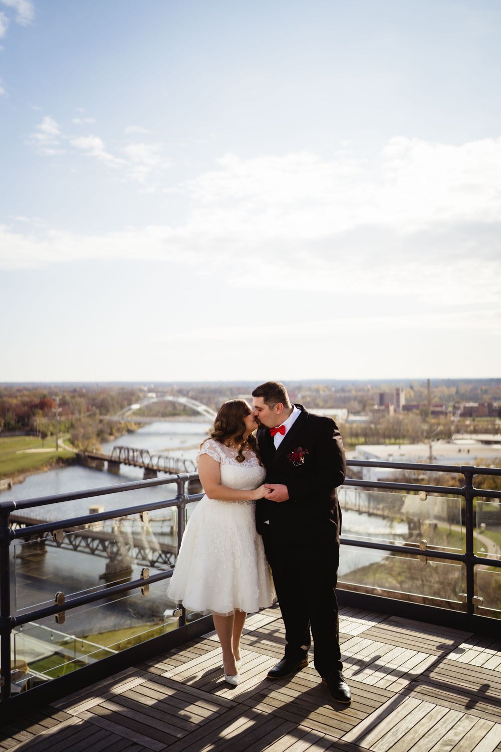 A couple in wedding attire shares a romantic dance on a balcony overlooking a winding river.