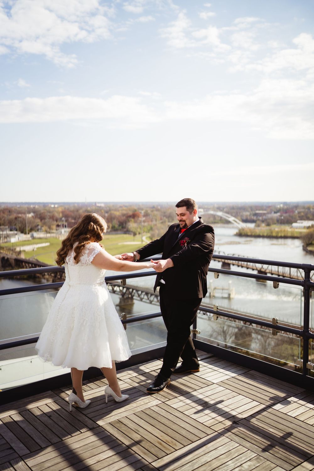 A couple in wedding attire dances on a wooden deck balcony with a scenic landscape behind them.