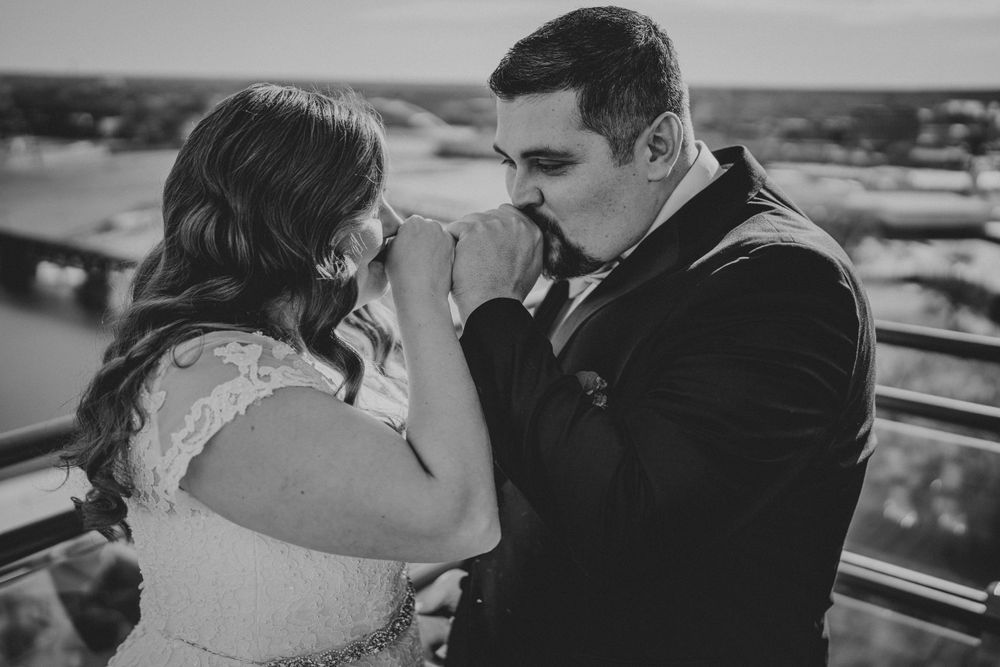 A tender black and white moment between a couple in wedding attire on a rooftop overlooking a city.