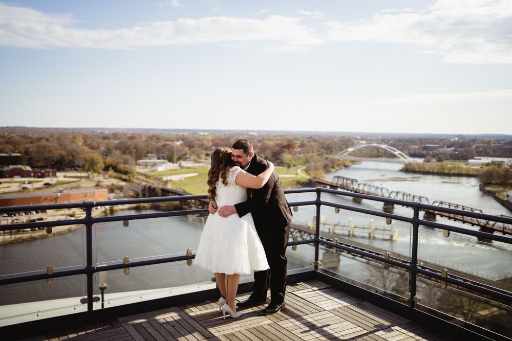 A romantic wedding couple embraces on an outdoor balcony with a scenic river view.