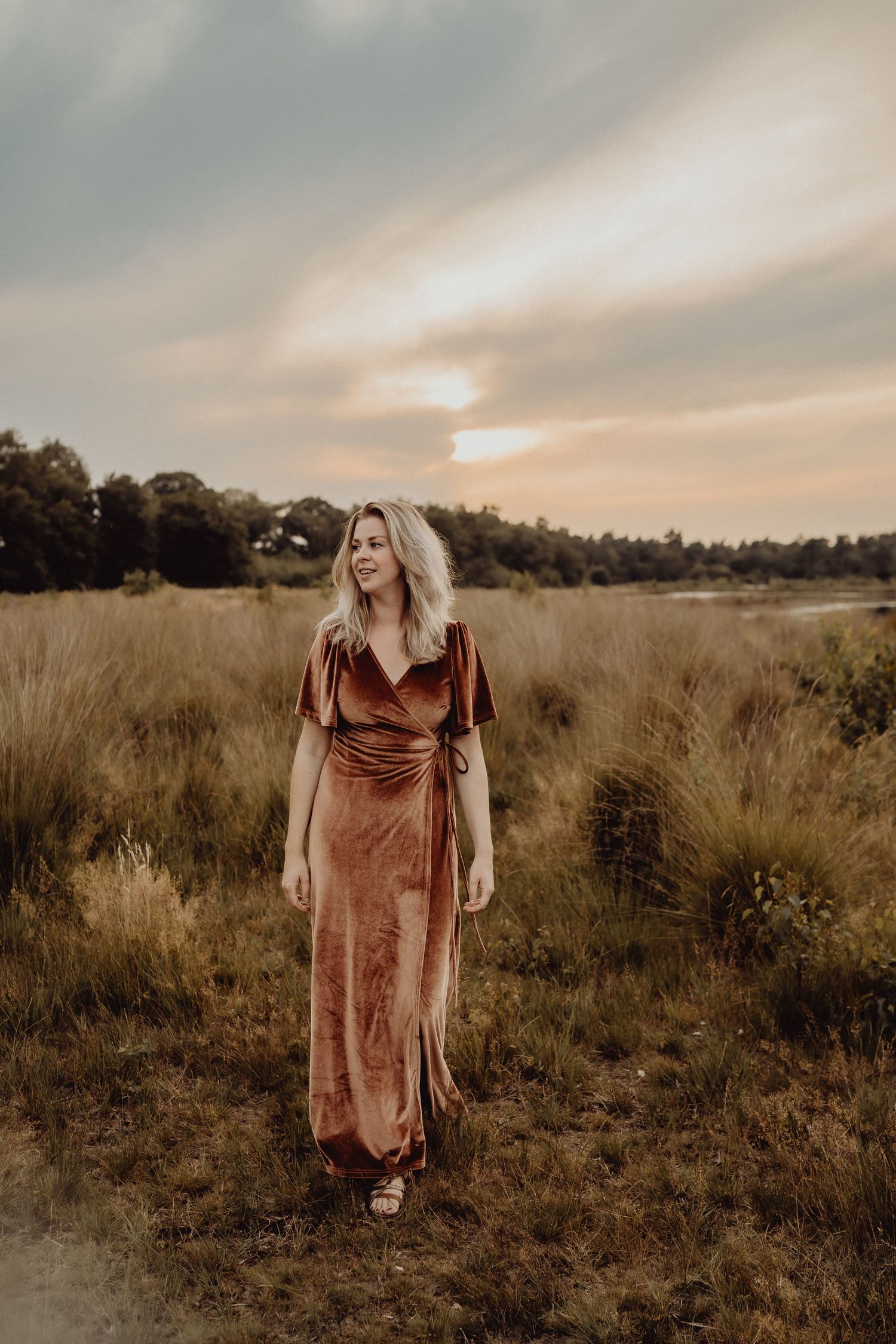 Woman in velvet maxi dress poses in rustic field during golden hour.