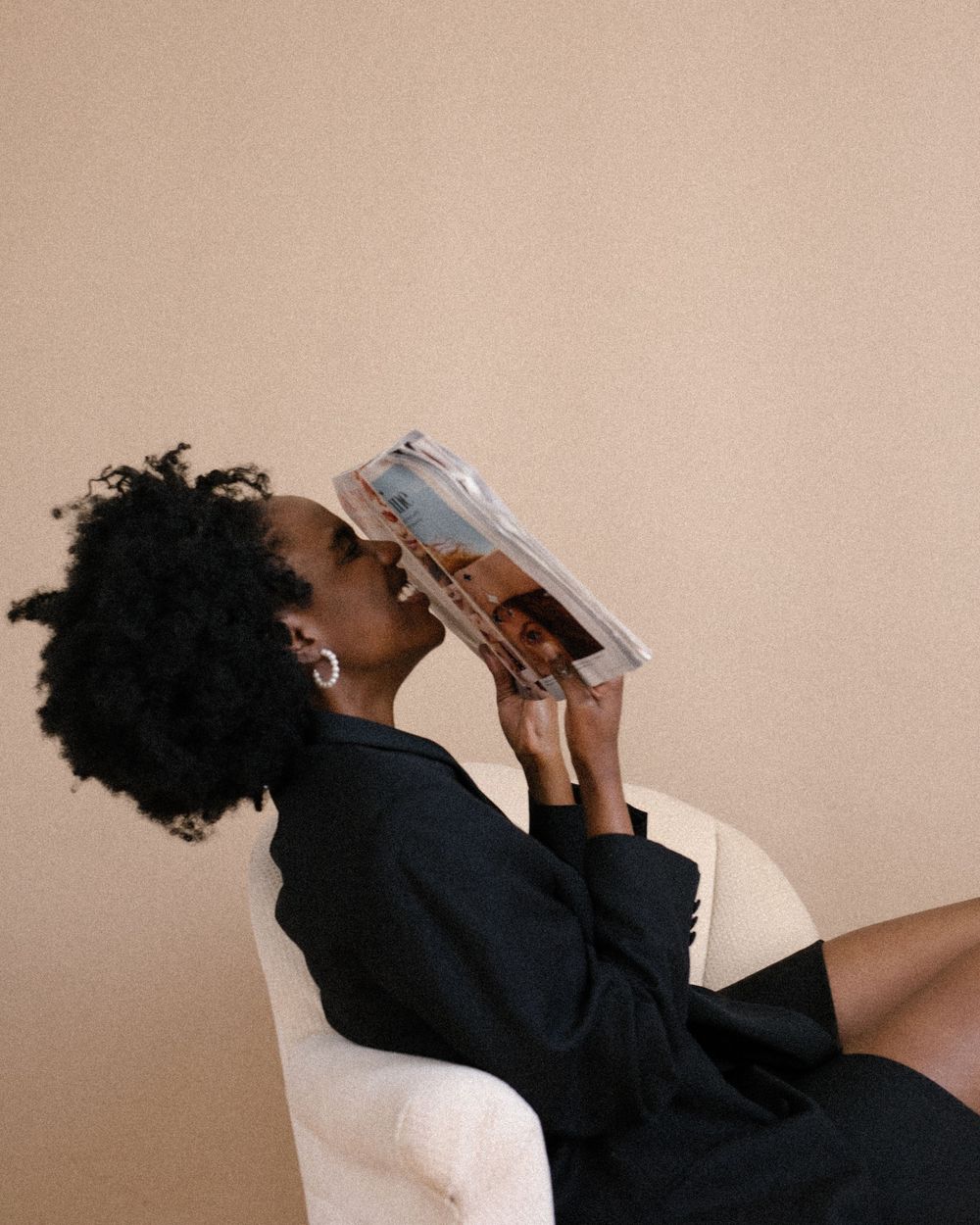 Creative shot of person with natural hair holding a book while reclining in white chair.