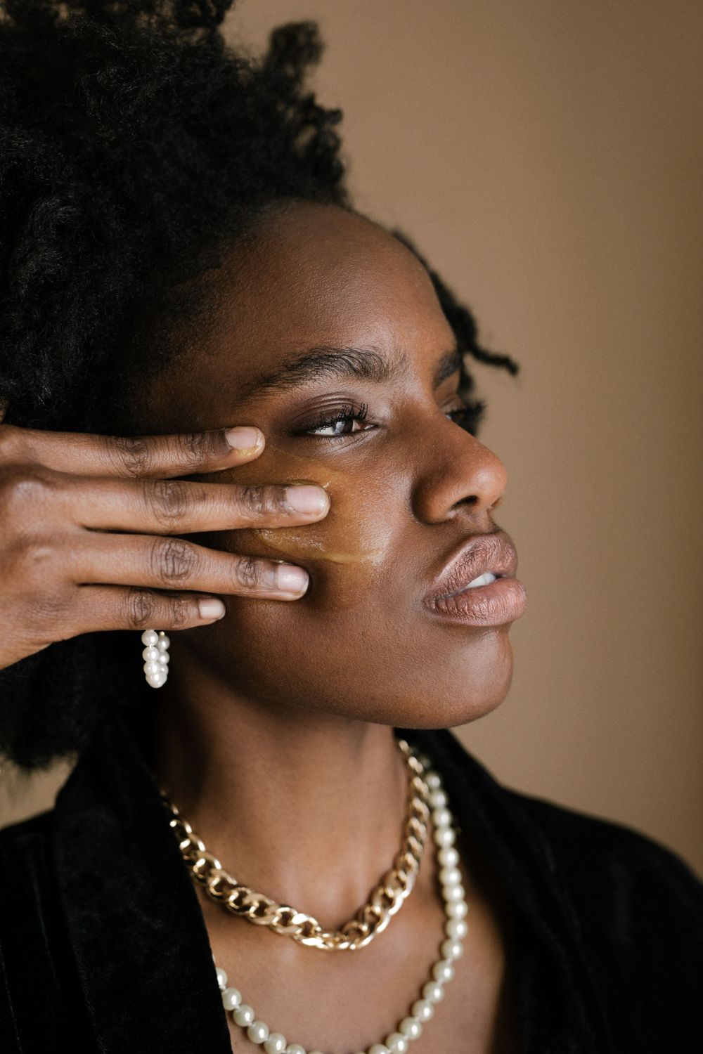 Side profile portrait featuring layered necklaces and delicate hand gestures against neutral backdrop.