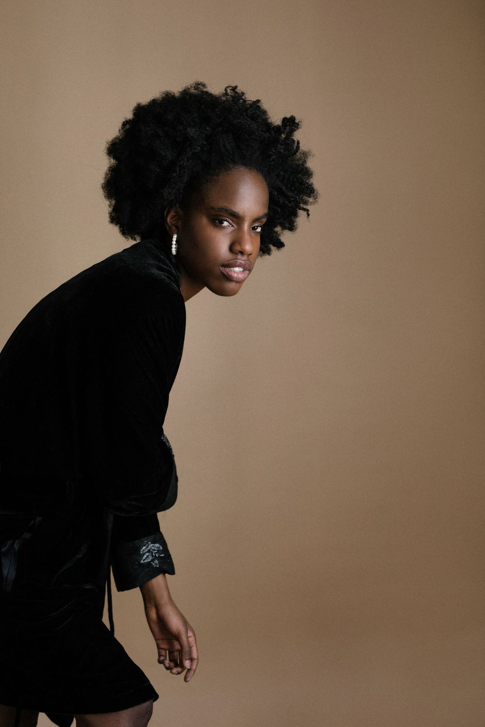 Artistic portrait in black velvet clothing against warm brown backdrop.