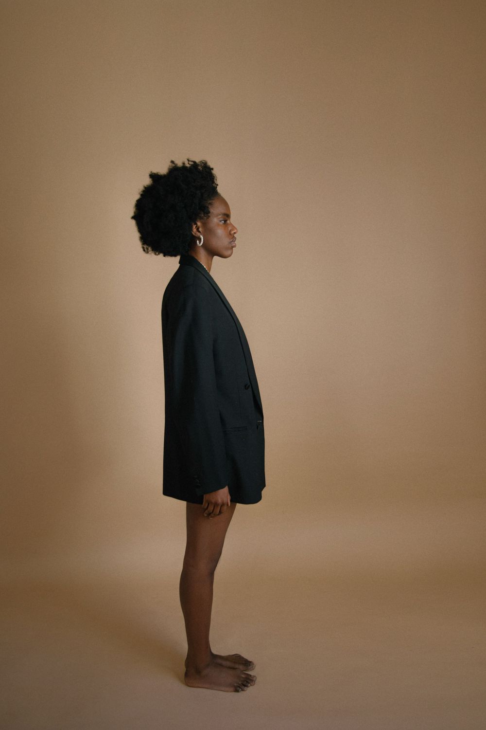 Minimalist full-length portrait in oversized black blazer against neutral backdrop.