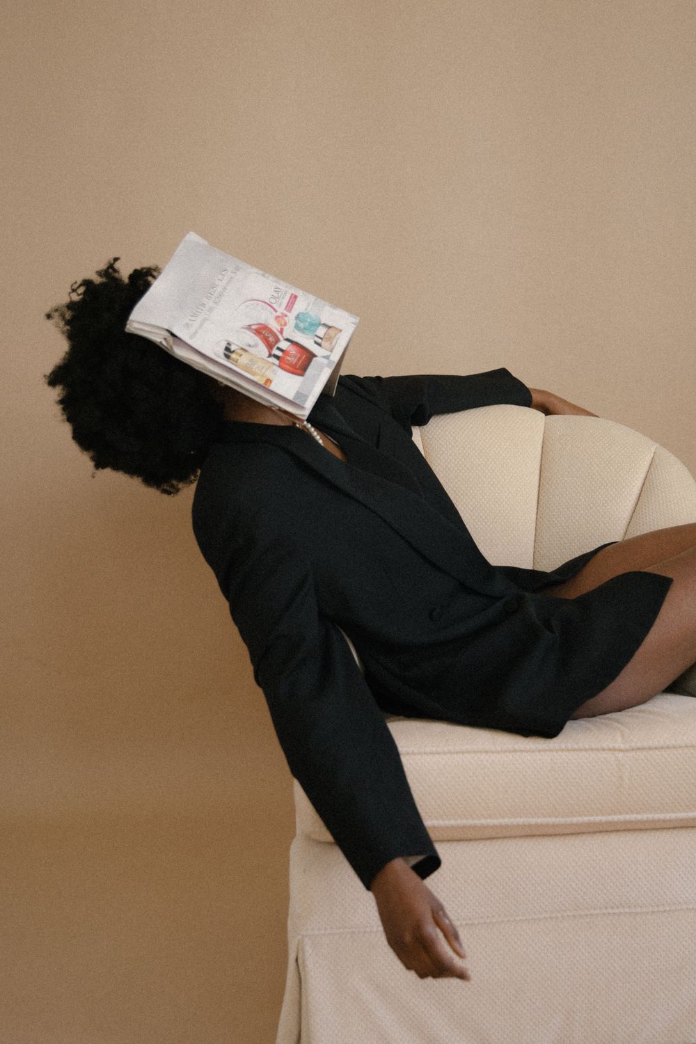 Artistic portrait of person relaxing with book on white chair wearing black blazer.