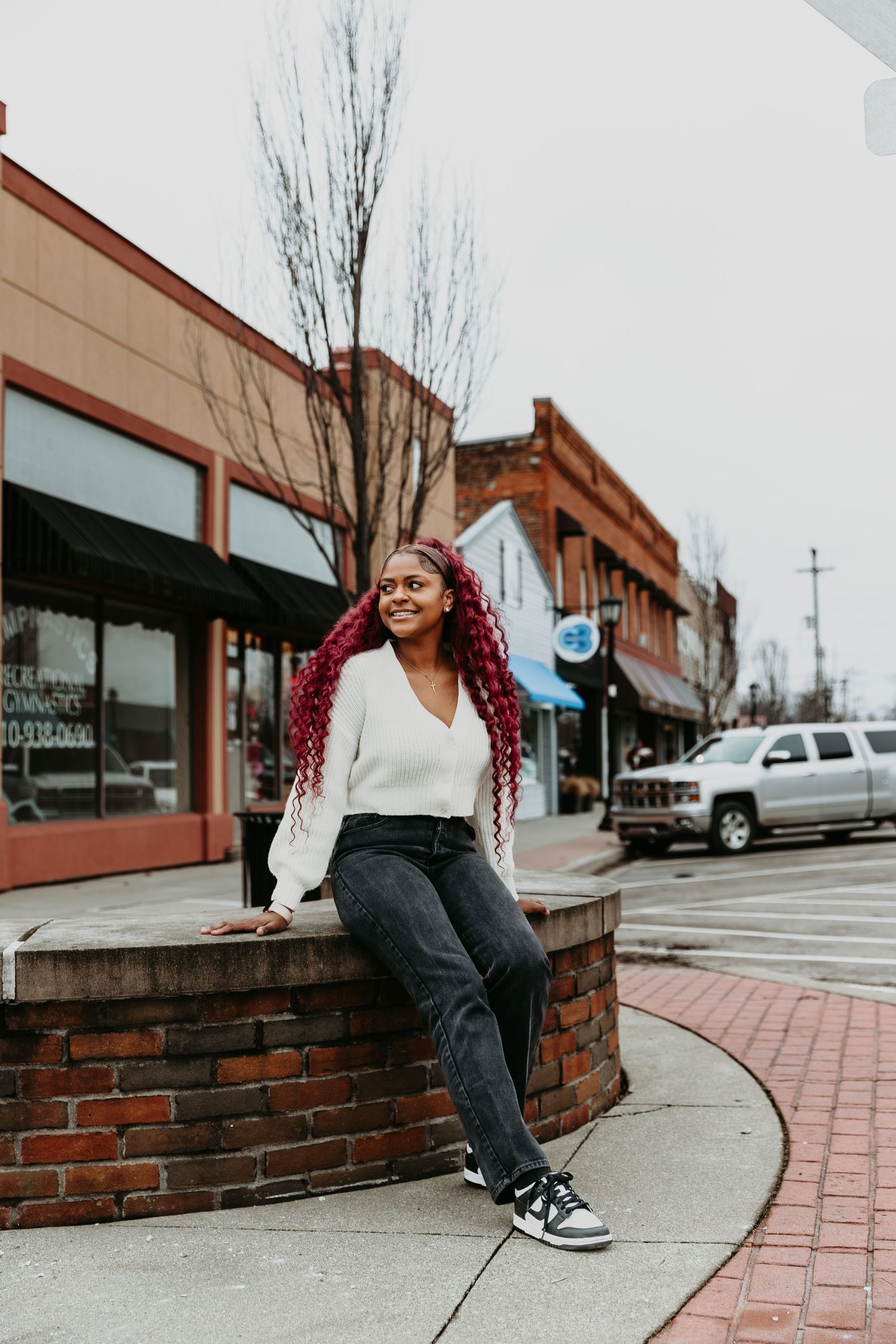 Street style portraits with model sitting on brick wall in casual outfit.