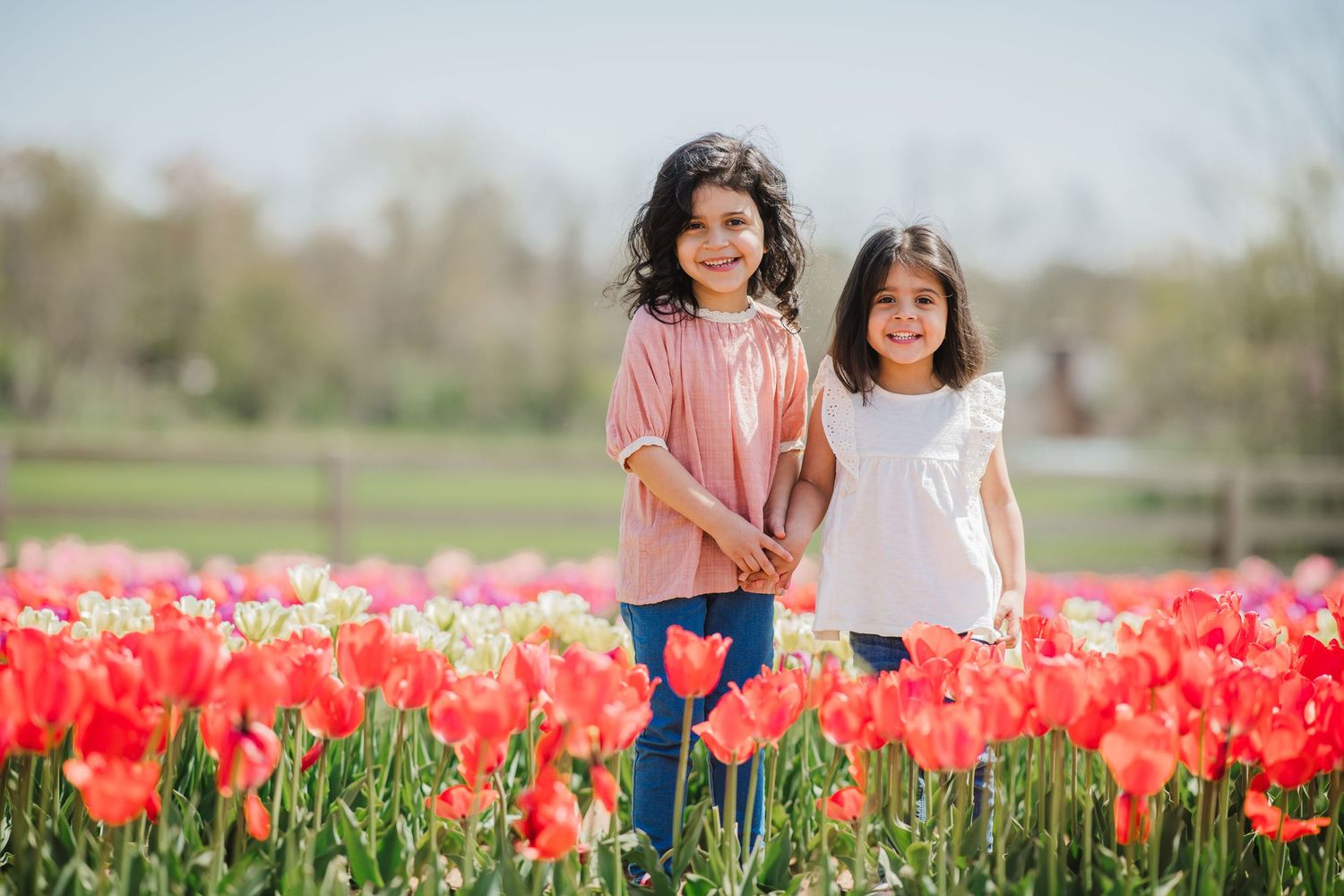 Two children stand together in a vibrant field of blooming red tulips during springtime.