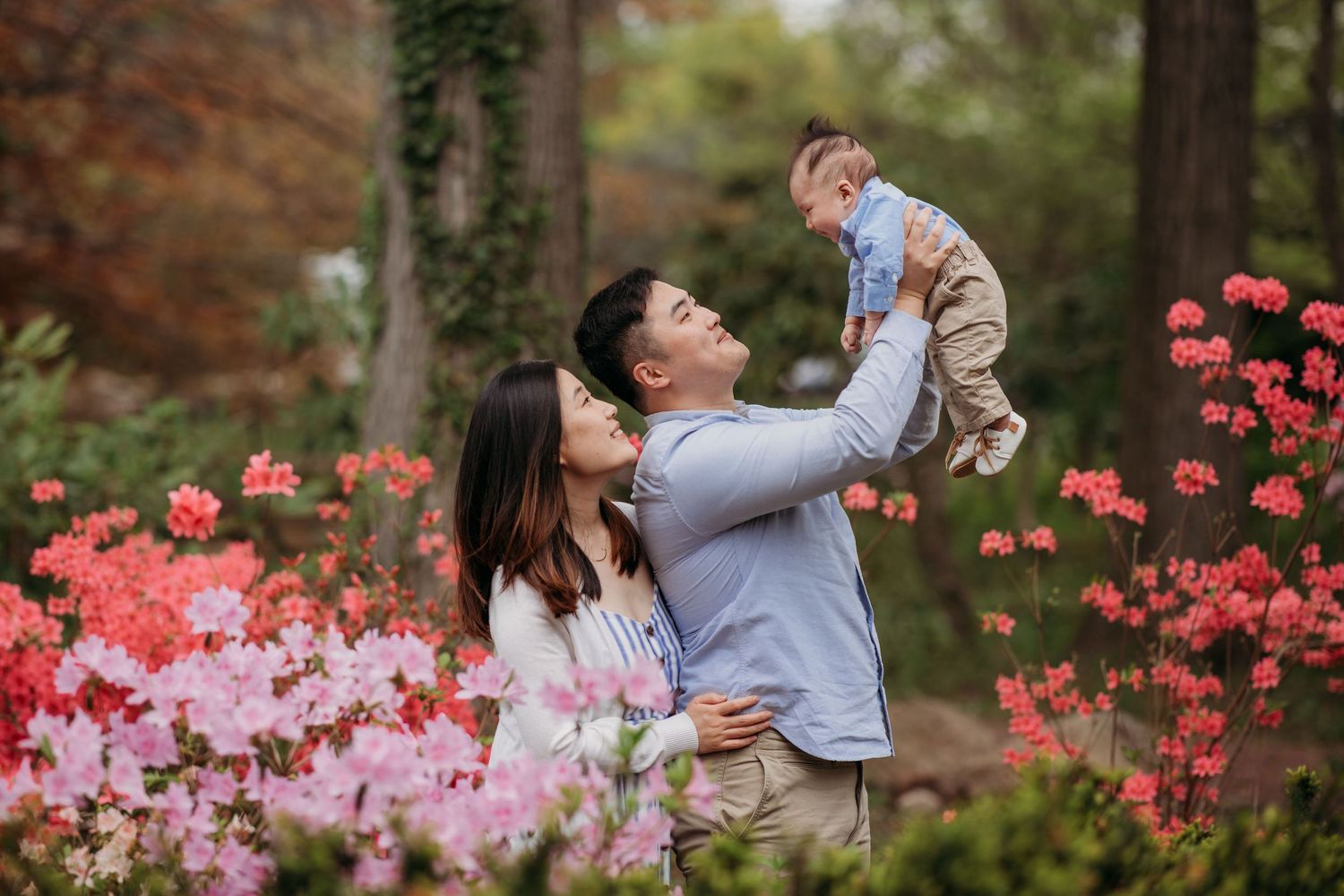 Family enjoying a joyful moment together in a garden with pink azalea flowers blooming in the background.